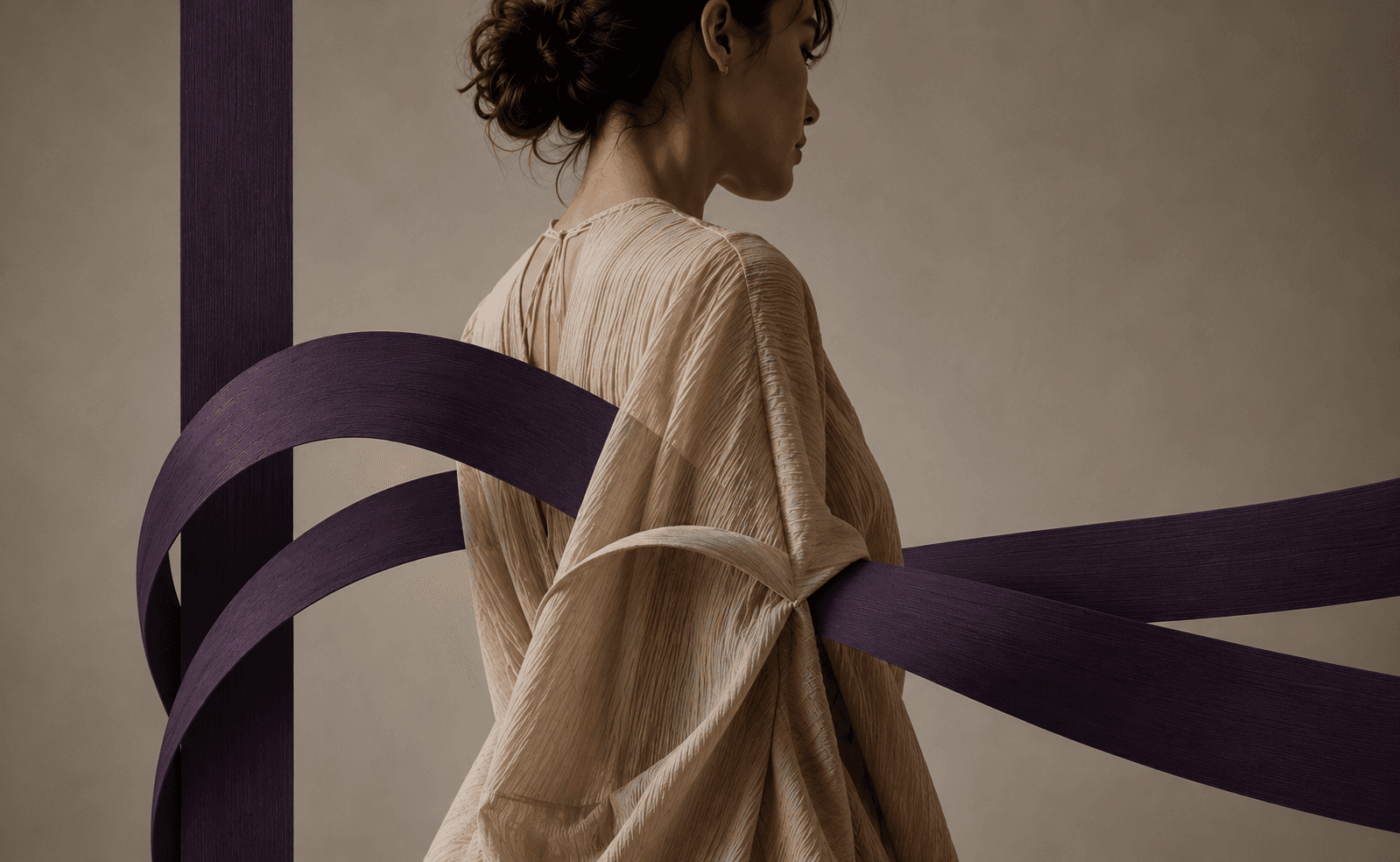 A designer in a textured ivory garment framed by a woven plum ribbon